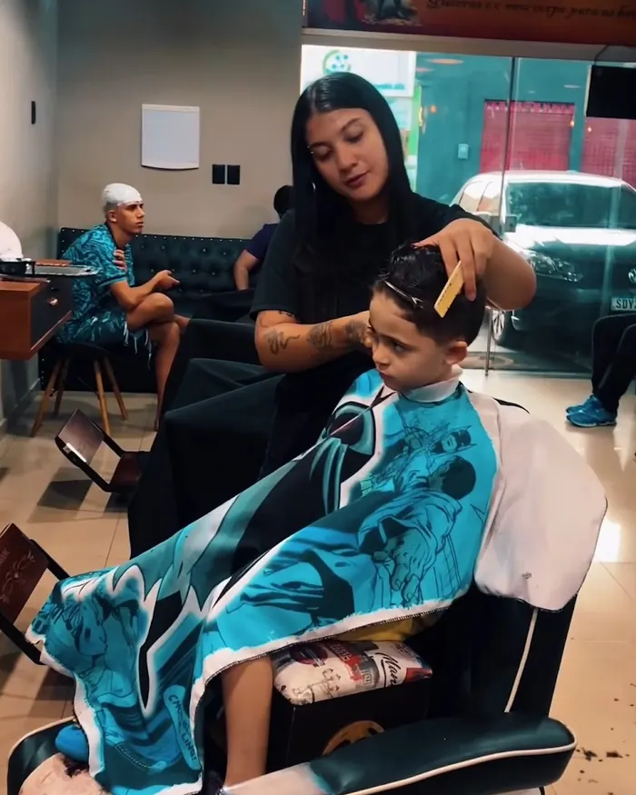 Barbeira cortando o cabelo de um menino na cadeira